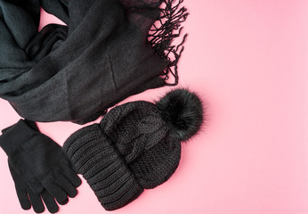 Flat lay winter or autumn warm woman accessories - black knitted scarf, hat on bright pink background, copy space