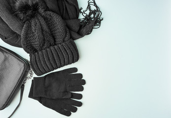 Flat lay winter or autumn warm woman accessories - black knitted scarf, hat, bag on bright blue background, copy space
