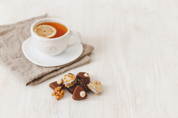 Cup of hot tea with lemon and chocolate candy with nuts on white wooden table, selective focus