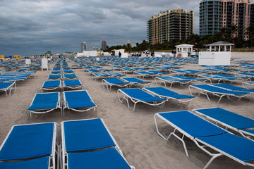 Blue sunbeds in neat rows in South Beach, Miami; stormy day, grey clouds.