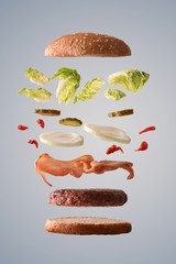 Beef burger floating with bacon onion and pickles gray background