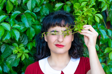 A beautiful woman covering her eyes with green leaves on a sunny day.