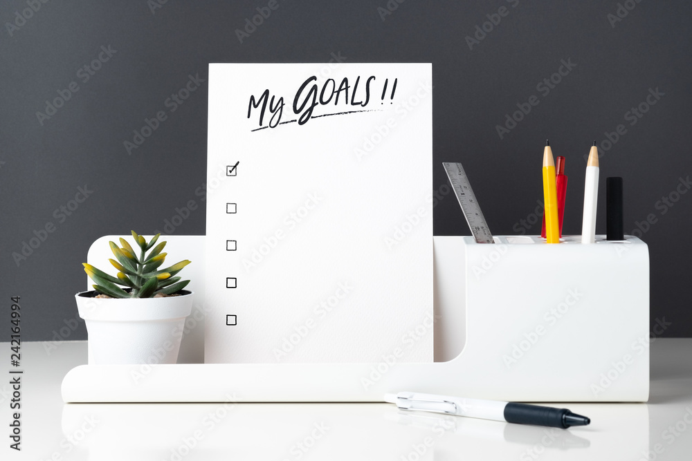 Poster my goals list on notepad at modern office stationery on white table and dark grey wall.pencil, notep
