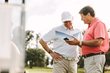 Senior golfers looking the scores on phone after the game - Powered by Adobe