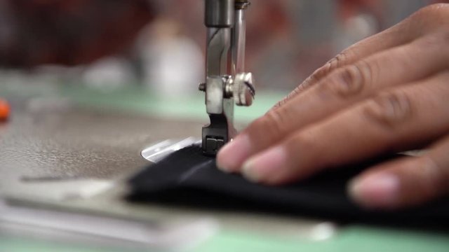 Close up seamstress using sewing machine stiching fabric together to create clothing.