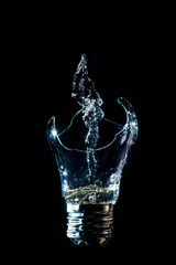 Creative broken light bulb with water fountain on isolated black background with flash