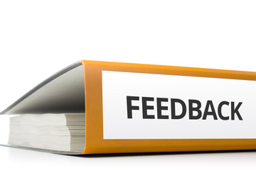 oranger Aktenordner gefüllt mit Papierseiten und Beschriftung Feedback liegend vor weißem...