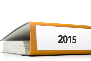 oranger Aktenordner gefüllt mit Papierseiten und Beschriftung 2015 liegend vor weißem Hintergrund