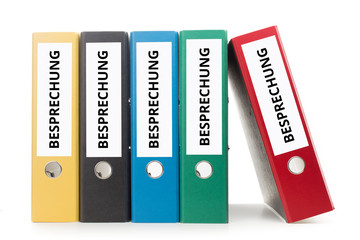 mehrere bunte Aktenordner dessen Ordnerrücken beschriftet sind mit besprechung stehend vor hellem...