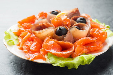 Gourmet restaurant serving a plate of smoked salt, raw white fish fillets and salmon. Delicacy fresh seafood dish with catfish, salmon meat with olives on a plate close-up