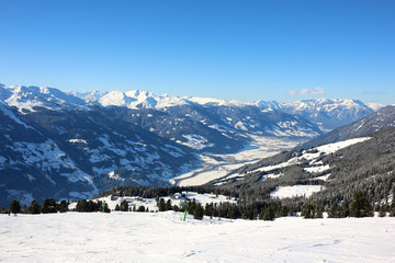 People enjoying skiing on prepared slopes in the Alps on sunny day. Beautiful snowy trees in the mountains. Perfect winter holidays destination for family in modern comfortable Alpine ski resort. 