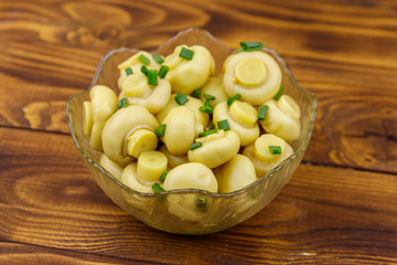 Glass bowl with pickled champignons. Marinated mushrooms on wooden table