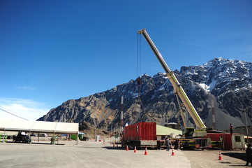 lifting maneuver with rental crane, modular red maritime container on a truck