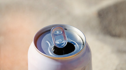 An aluminum beer can stands on the hot sand of the beach