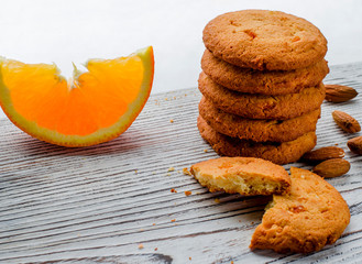 Round orange biscuits with colorful candied fruits and a slice of juicy orange lying on a wooden table against the background of winter forest