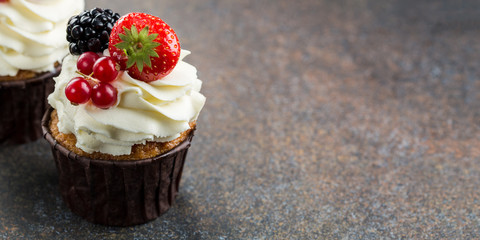 Various sweet berry cupcakes on brown stone background. 