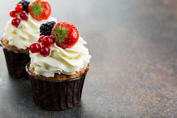Various sweet berry cupcakes on brown stone background. 