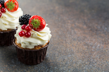 Various sweet berry cupcakes on brown stone background. 