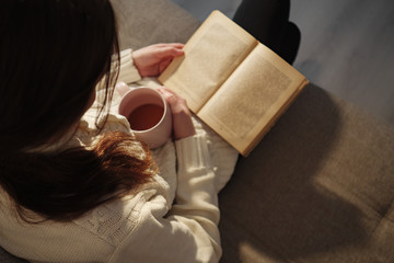 top view of woman holding cup of tea and reading book