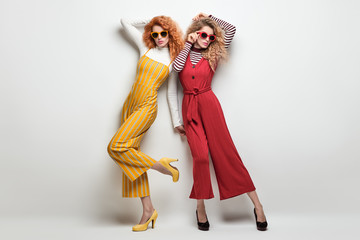 Fashion Young Cheerful Blond Redhead Lady in Colorful Outfit. Two Sensual Model Girl Having Fun in Studio. Trendy Hairstyle, makeup. Portrait Woman Friends, fashionable Style