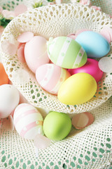 Naklejka na ściany i meble A beautiful and colorful close-up flat of easter eggs in plain colors and striped in a basket with flowers