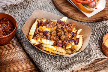 Close up view on traditional american fast food. French fries with bacon and salsa sauce on brown background. Copy space for text logo or brand.