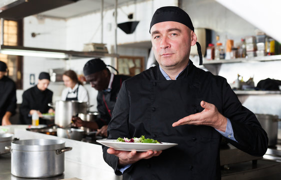 Positive male cook with cooked dish in restaurant kitchen