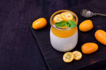 Creamy panna cotta and orange jelly in a glass jar topped with kumquats and mint against the dark background, Two layered dessert