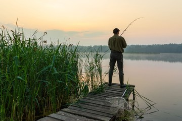 Angler catching the fish from wooden pier during dawn