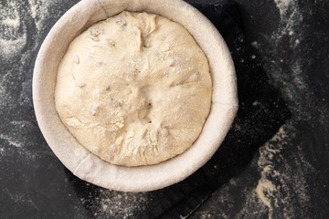 Baking bread. Dough in proofing basket on table with flour, sunflower seeds. Top view.