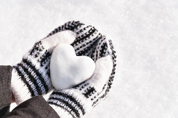 Female hands in knitted mittens with heart of snow in winter day. Love concept. Valentine day background.