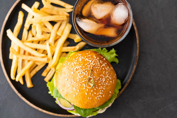 Tasty grilled home made burger with beef, tomato, cheese, cucumber, french fries and lettuce on a dark stone background with copy space. Top view. fast food and junk food concept