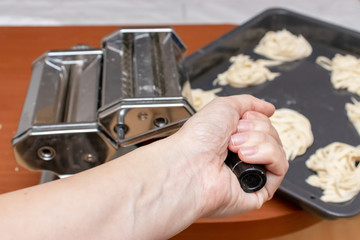 Hand holding a handle of rolling dough machine fo making pasta and ravioli close up with homemade ribbon egg italian pasta on background