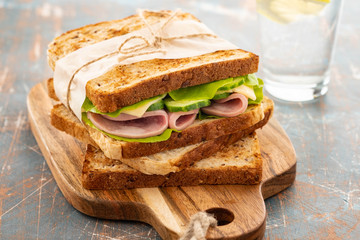 Close-up photo of a club sandwich. Sandwich with meet, prosciutto, salami, salad, vegetables, lettuce on a fresh sliced bread on wooden background. Copy space.