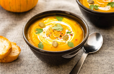 Pumpkin soup with pumpkin seeds on a bowl on linen textile background, top view. Autumn concept.