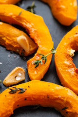 Cooked pumpkin pieces with garlic and rosemary on a black plate. Copy spase.