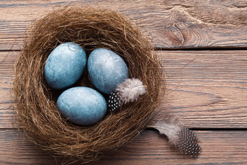 Three marble blue Easter eggs, in a nest with feathers on a wooden background. The Symbol Of Easter. Copy space