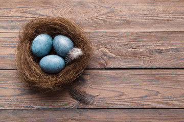 Three marble blue Easter eggs, in a nest with feathers on a wooden background. The Symbol Of Easter. Copy space