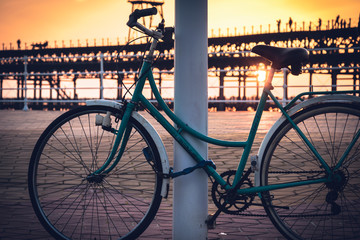 With the background of a sunset on the Rio Tinto dock, a vintage bicycle remains tied to a pole in Huelva, Andalusia, Spain