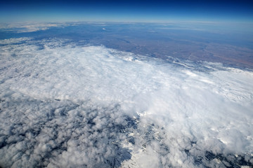 Winter landscape with snow, land and clouds view from flying airplane from a great height above clouds