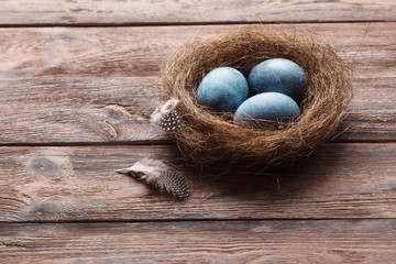 Three marble blue Easter eggs, in a nest with feathers on a wooden background. The Symbol Of Easter. Copy space