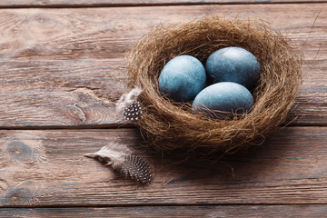 Three marble blue Easter eggs, in a nest with feathers on a wooden background. The Symbol Of Easter. Copy space