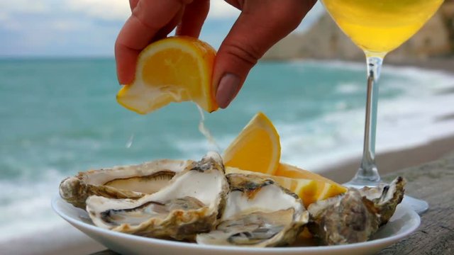 Hand squeezes lemon juice on fresh oysters against the background of ocean waves on the quay Etretat, Normandy