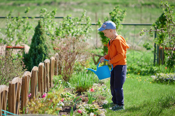 Cute European boy is watering flowers in the countryside croft. He is enjoying his job. © Artem