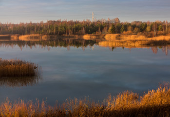 beautiful natural landscape with sun-flooded lake, small mountain with trees; a blue sky and a wonderful reflection of trees and sky in the water