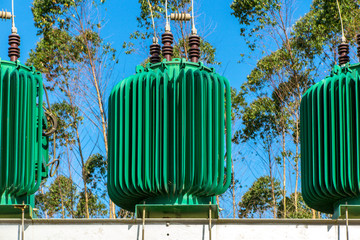 Close up on green colored energy transformer in metal structure, trees and blue sky in background,...