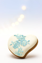 Gingerbread heart-shaped in white glaze and floral pattern on bokeh background from the garland