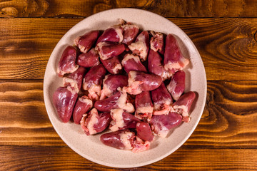 Ceramic plate with raw chicken hearts on wooden table. Top view