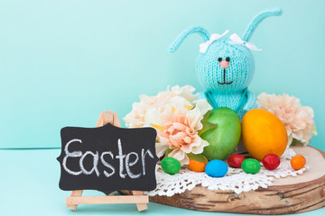 Easter celebration. Cute handmade knitted hare - a symbol of the holiday. Near her are colored eggs and Easter cake. Free space for text. Greeting card.