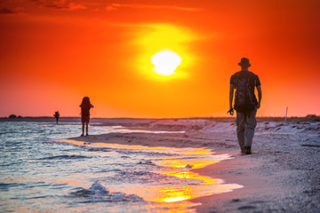 Tourist hike along the sea surf in the rays of the summer sun at sunset